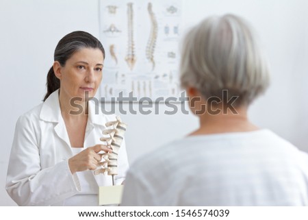 Aging and back pain concept: doctor of orthopedics showing her senior patient a slipped disk on a backbone model. Royalty-Free Stock Photo #1546574039