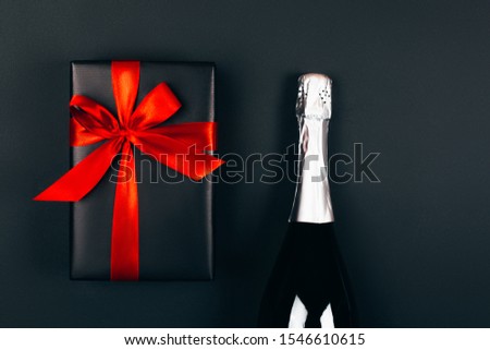Champagne with present box on dark background. Festive concept. Flat lay style. Black box with red bow.