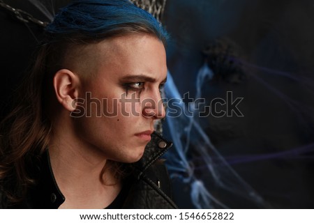 Teen alt boy with blue hair and shaved head dressed in black on dark background