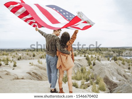 Happy young couple holding a waving American flag in nature. Independence Day, lifestyle, travel concept.