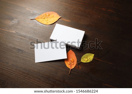 Photo of blank business cards and autumn leaves on wood table background. Template for branding ID.