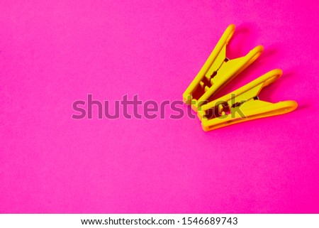 two colored yellow clothespins lie on a pink background