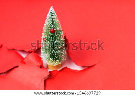 Small decorative Christmas tree isolated on red paper hole breakout background. Festive Christmas background.