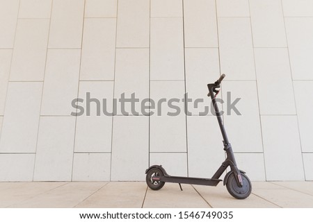 Black stylish electric scooter standing against a concrete wall on a sunny day. Environmentally friendly transport