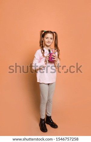 smiling girl with a felt-tip pens stands on a pink background in daily clothes; full-length; photo