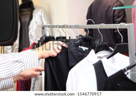 A woman chooses clothes in a store. A variety of women's clothing on hangers. Photo without a face. Hands close up.