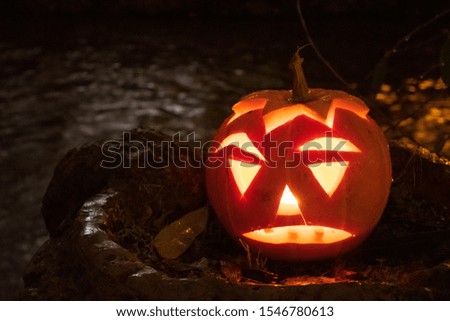 Spooky Halloween pumpkin, Jack O Lantern, with burning candles, and dark scary river on background