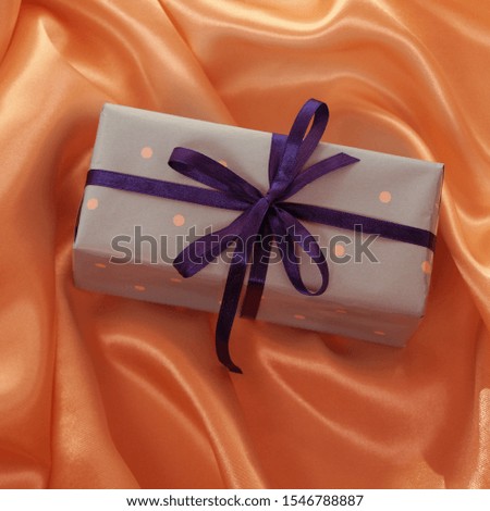 gift in colored paper, tied with satin ribbons on a luxurious texture of satin, silk with waves, folds and highlights, congratulatory, holiday concept, horizontal, close-up, copy space