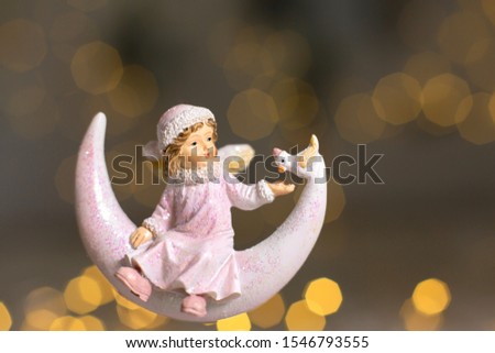 Decorative figurines of a Christmas theme. Statuette of an angel on a crescent moon. Christmas tree decoration. Festive decor, warm bokeh lights
