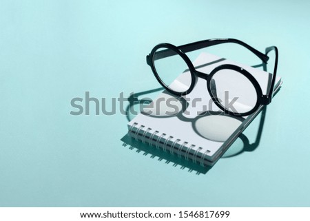 black round glasses lie on a Notepad and cast a shadow on the mint background