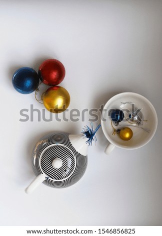 three small Christmas balls in a mug, next to three large balls and a glass teapot from which tinsel is visible. Christmas advertising. extraordinarily