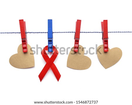 Hearts cut out of kraft paper and red awareness ribbon hang on natural twine attached with clothespins. Isolated on white. World AIDS day concept. 