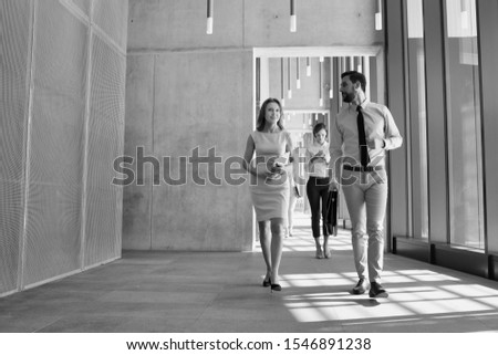 Black and white photo of business people walking while discussing plans before meeting in office corridor
