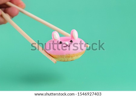 Chopstick holding a cute pink mini rabbit donut on green background