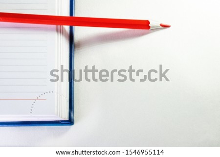 a red pencil lies on the open blue notebook paper on white background