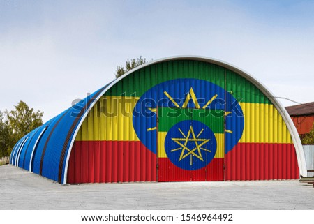 Close-up of the national flag of Ethiopia painted on the metal wall of a large warehouse the closed territory against blue sky. The concept of storage of goods, entry to a closed area, logistics