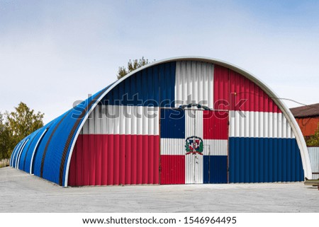 Close-up of the national flag of Dominicana painted on the metal wall of a large warehouse the closed territory against blue sky. The concept of storage of goods, entry to a closed area, logistics