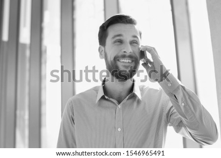 Black and white photo of businessman smiling while talking on smartphone during break in office