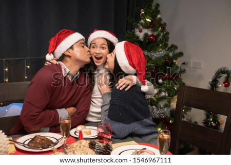 happy family, father and mother kissing daughter together, daughter happy and smiling, celebrate at christmas day night in dining room that decorated with christmas tree for christmas festival day