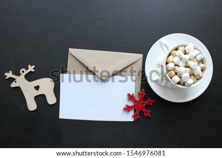 A Cup of cocoa with marshmallows and an empty envelope on the background of a Christmas tree and Christmas tree toys, a wooden deer, cinnamon sticks. Christmas background, bokeh, copy space.