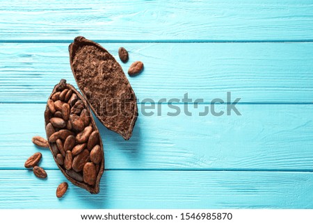 Halves of cocoa pod with beans and powder on blue wooden table, top view. Space for text