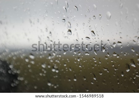 Macro photo of a window in rain drops against blurred gray autumn landscape 