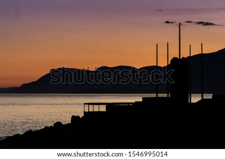A silhouette of a building near the sea with a mountain and a beautiful sky in the background at sunrise