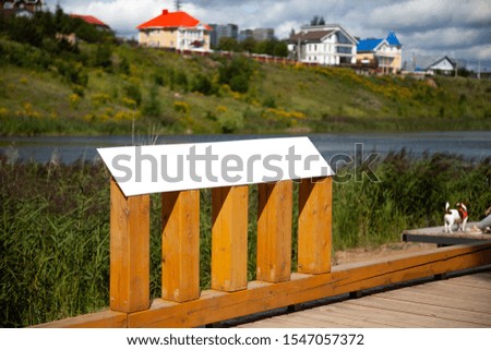 Blank horizontal information sign on wooden stand in park in front of a lake