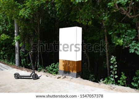 Blank vertical information sign on wooden stand in park with electric scooter nearby