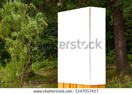 Blank vertical information sign in park in front green forest on wooden stand