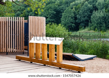 Blank horizontal information sign in park on wooden stand in front of a lake
