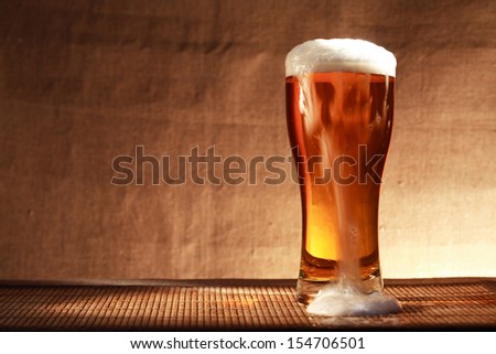 Full glass of freshness beer with foam on table against gray canvas background