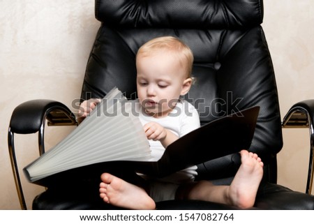 child examines and plays with a folder for documents, sitting in a large office chair