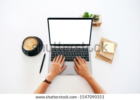 Top view mockup image of hands using and typing on laptop with blank white desktop screen on the table