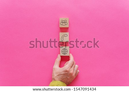 Male hand placing three wooden blocks with contact and information icons on them over pink background. With copy space.