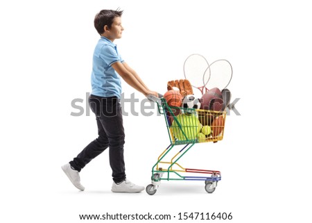 Full length profile shot of a boy walking and pushing a mini cart with sport items isolated on white background