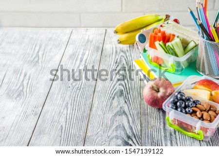 Healthy school lunch box. Kid's lunch box with sandwiches, fruit, vegetables, nuts, water and school supplies, White wooden background