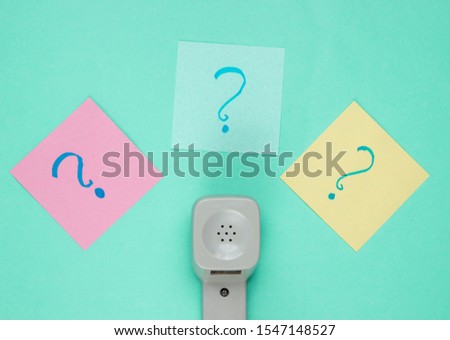 Retro handset and question marks on memo pieces of paper. Call center. Hotline. Blue studio background, top view.