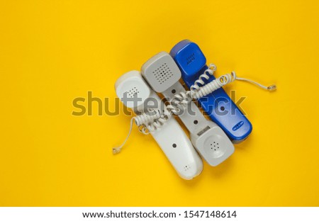 Three office phone tubes wrapped in cable on yellow studio background. Call center, hotline concept