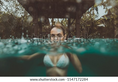 Beautiful woman having a bath in the swimming pool while it s raining