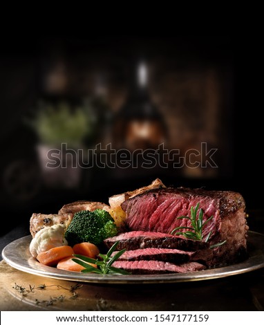 Succulent side of rare roast beef with seasonal vegetables, Yorkshire Puddings and roast potatoes with Rosemary garnish shot in a rustic setting with an old fashioned wood burner. Copy space. Royalty-Free Stock Photo #1547177159