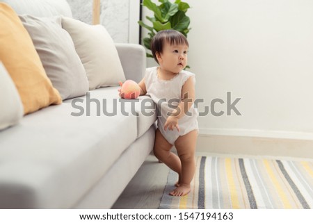 Little girl stands near the sofa at home