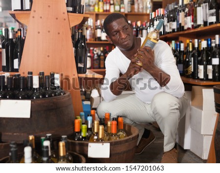 Portrait of young African American man visiting winehouse searching bottle of the good wine 