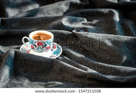 Cup of Turkish coffee with a traditional oriental pattern. Dark fabric background. Copy space. Top view. Selective focus image.