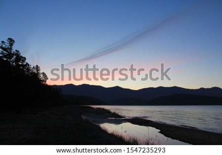 A scenic landscape - summer sunset in a Zmeyevaya Bay (Snake Bay), peninsula Svyatoy Nos (Holy Nose), Baikal Lake. Sky colored in light blue, pink and purple hues with sun setting over the mountains