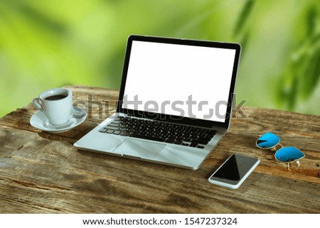 Blank screens of laptop and smartphone on a wooden table outdoors with nature on background, mock up. Cup of coffee near by. Concept of creative workplace, business, freelance. Copyspace.