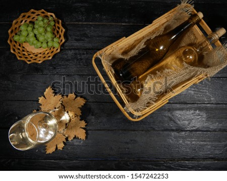 Bottles of expensive white wine on black background. Top View.
In rich restaurant white wine bottles on table. Nearby are: full glass with white wine, green grapes.