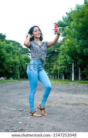 Charming teenager dressed in a black blouse with small white flowers and blue trousers taking a picture of herself with her smart phone. Concept of feminine beauty. Vertical image