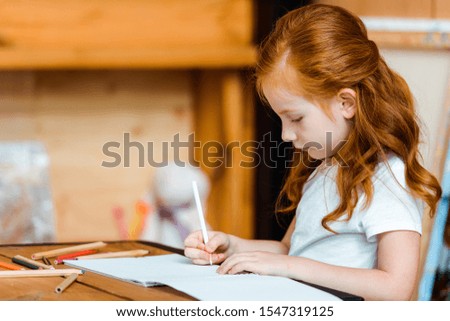 cute redhead kid drawing on paper in art school 