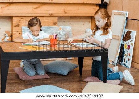 cute kids drawing on papers while sitting on pillows 